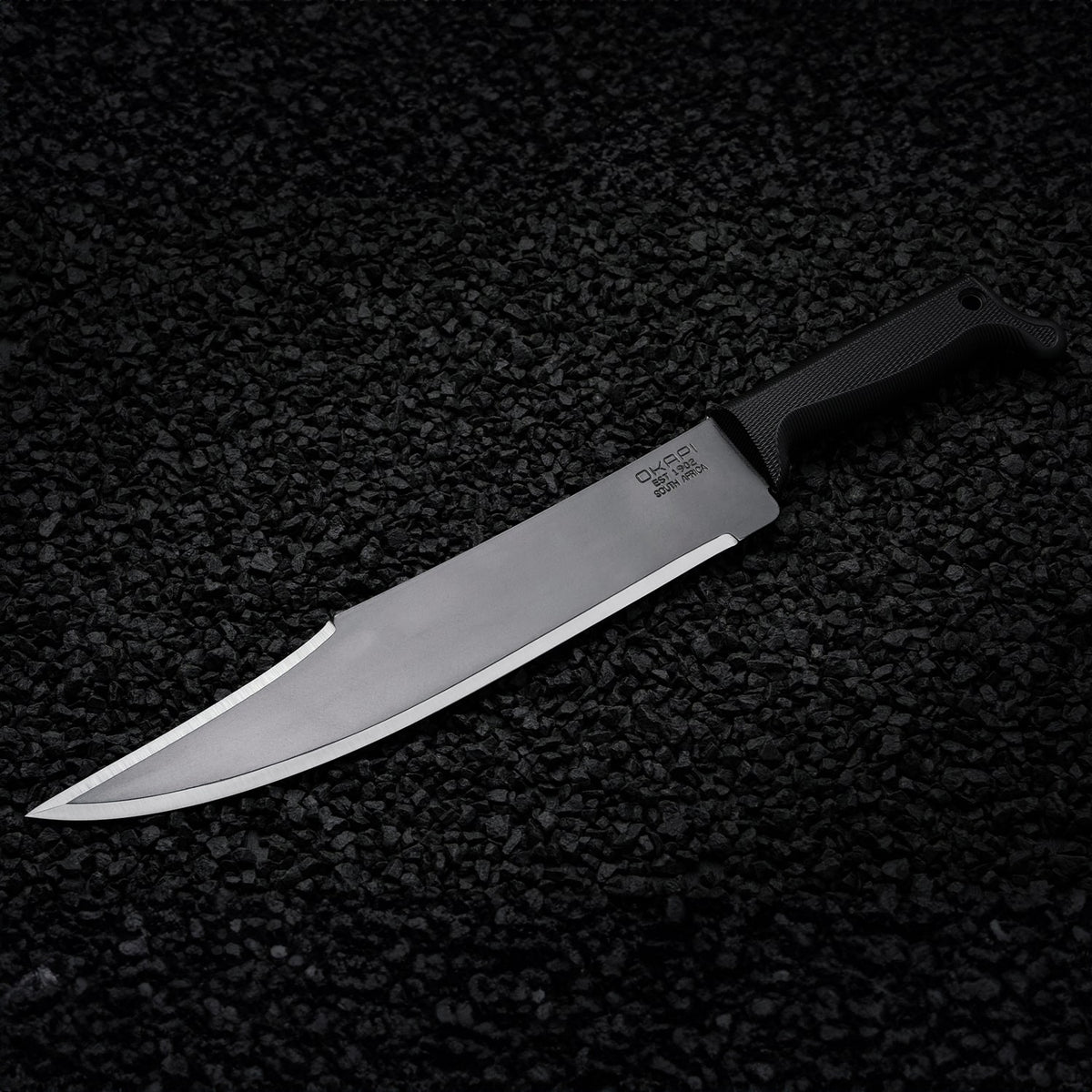 Okapi Bowie machete featuring Tactical Black handle shown on black stone ground