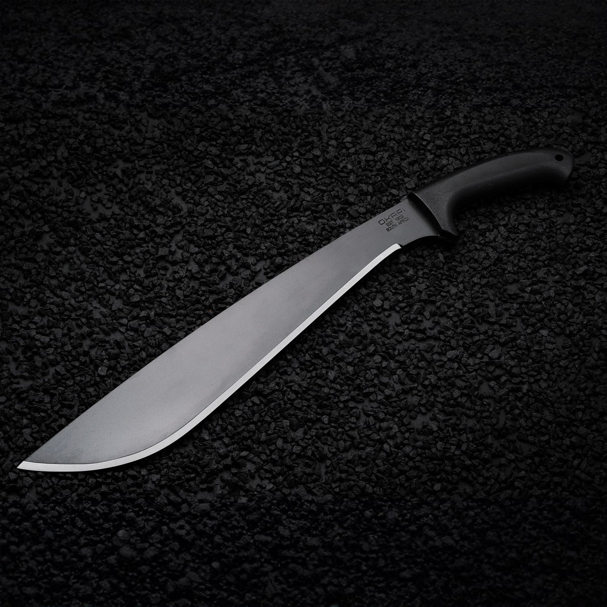 Tactical Okapi Jungle machete resting on black rock floor in lifestyle scene