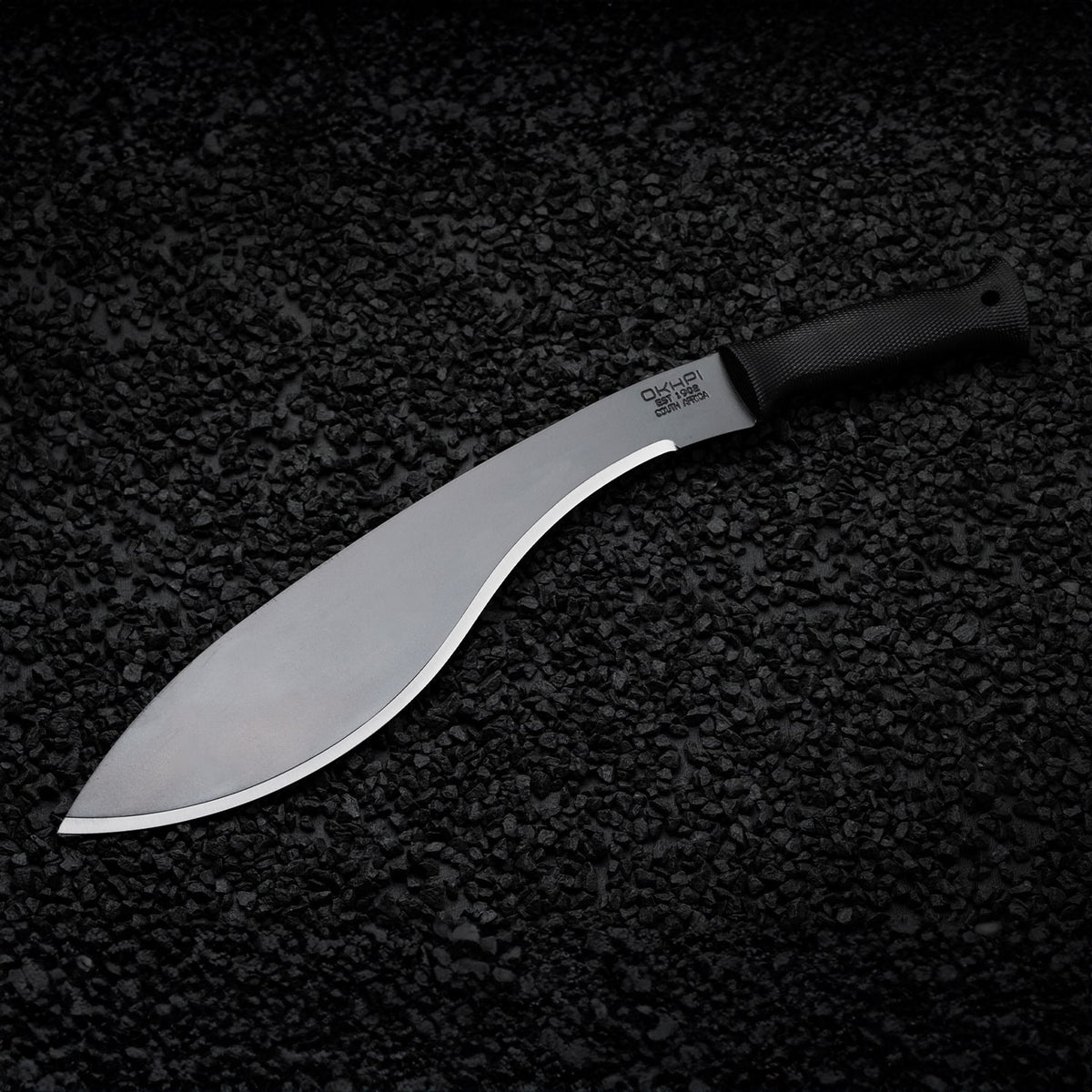 Curved Okapi Kukri machete with black grip featured on rugged rock floor scene