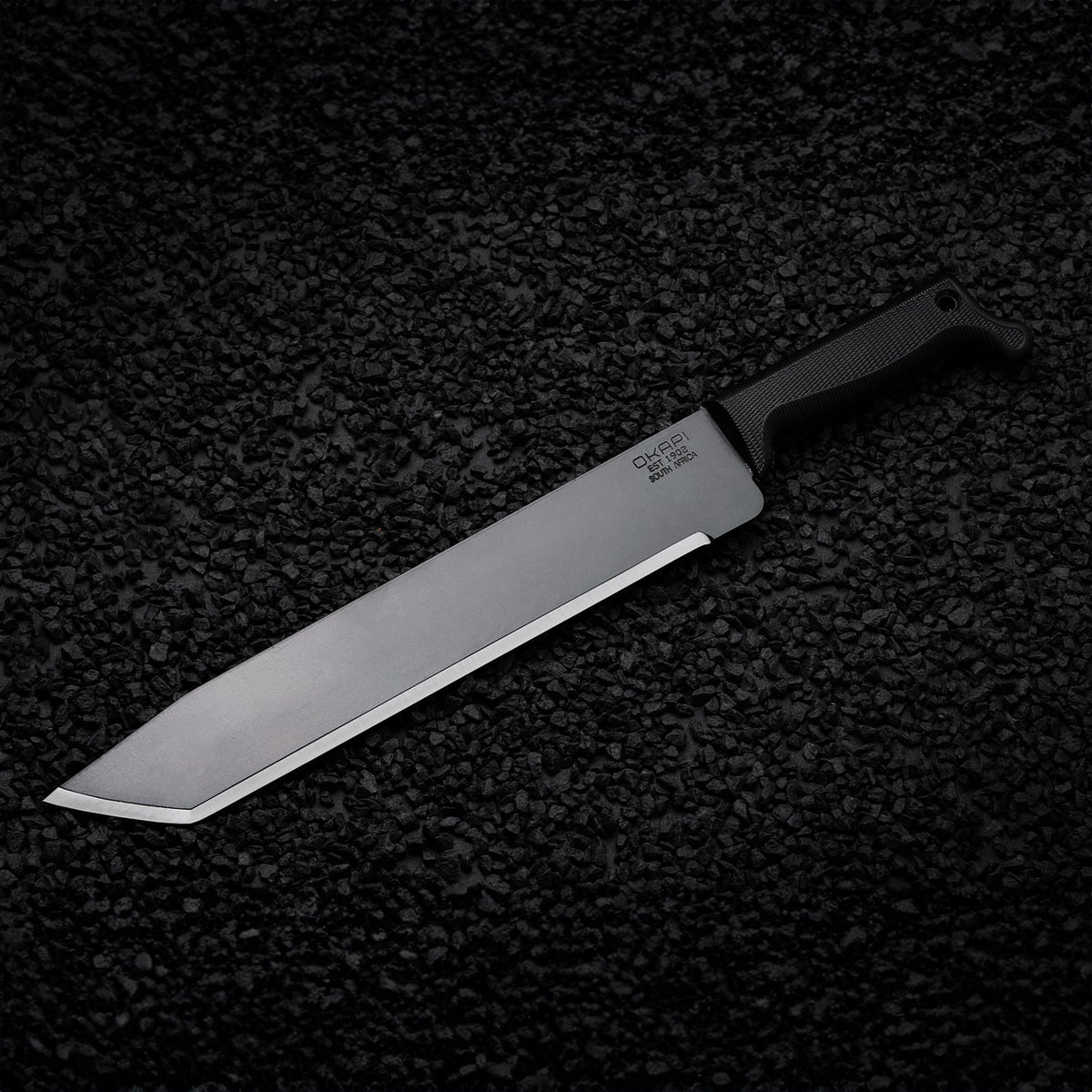 Tanto-style Okapi machete featuring a Tactical Black handle on black stone floor