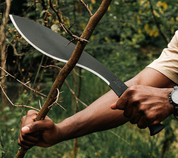 Okapi Kukri machete featuring distinctive curved blade and Tactical Black handle in nature scene